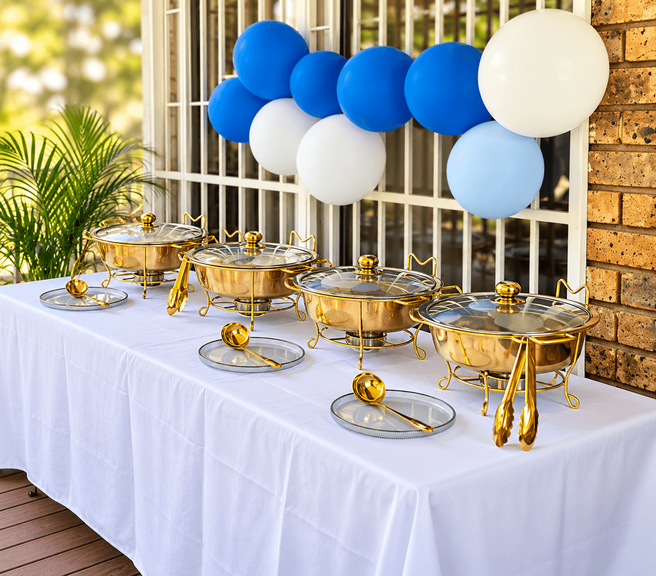 Gold chafing dishes on a white buffet table beneath a blue and white balloon garland