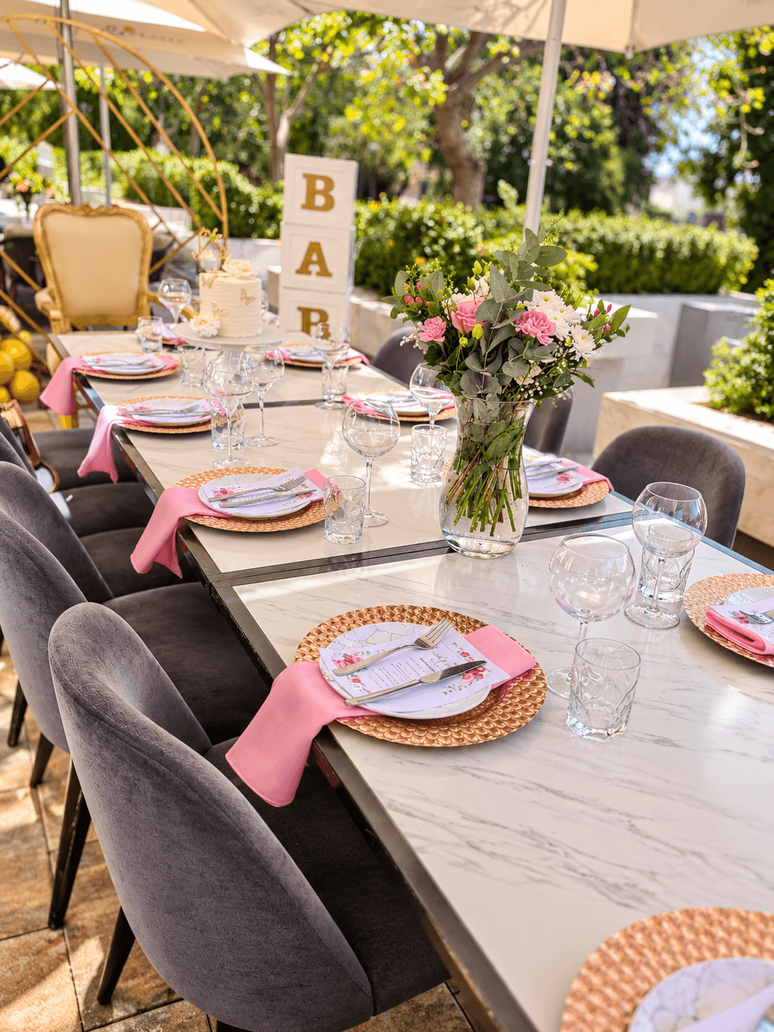 Outdoor baby shower table with rose-gold chargers, pink napkins, fresh flowers and BABY letter blocks