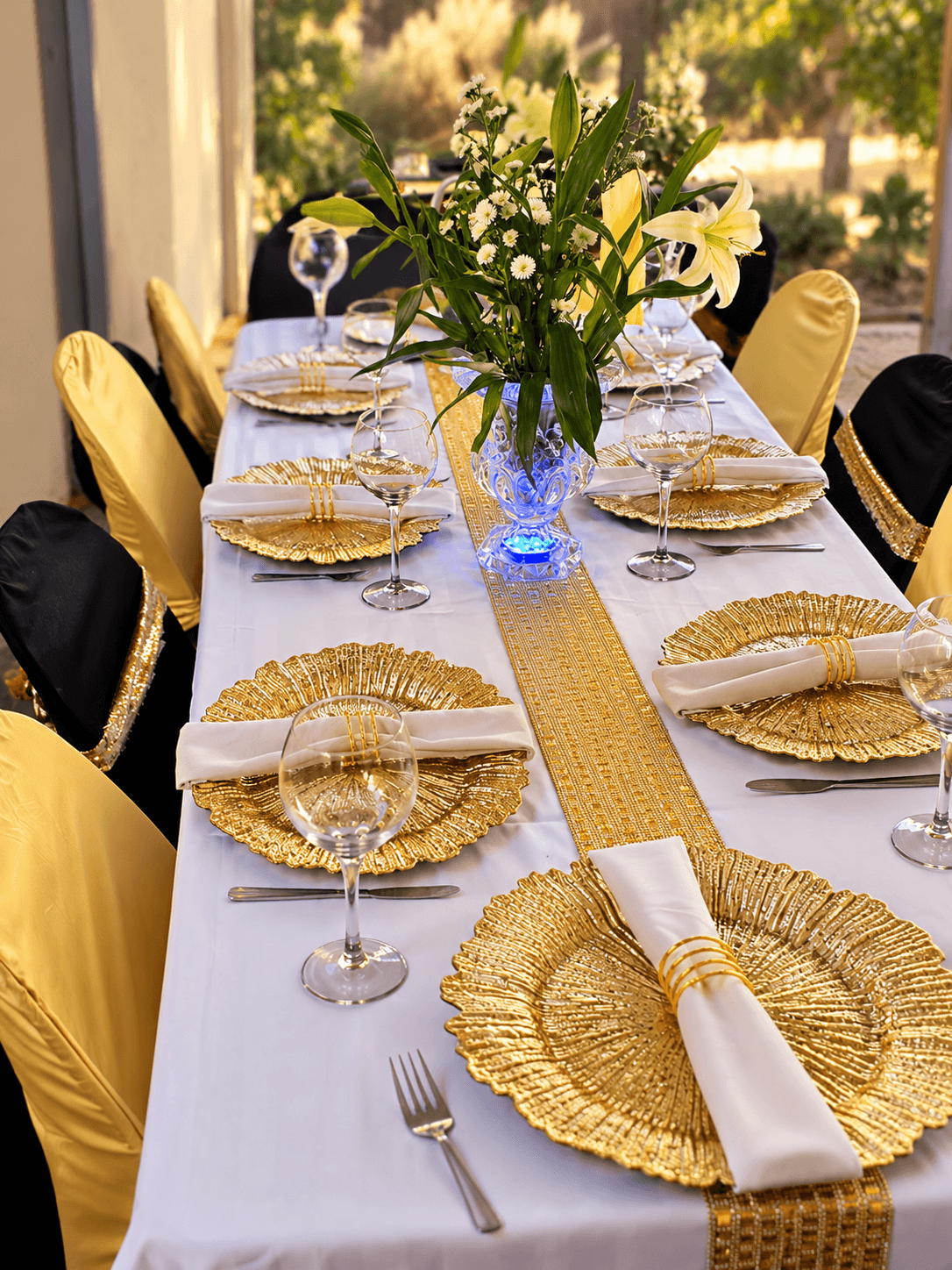 Long table with gold charger plates, white napkins in gold rings, a gold runner and a lily centrepiece
