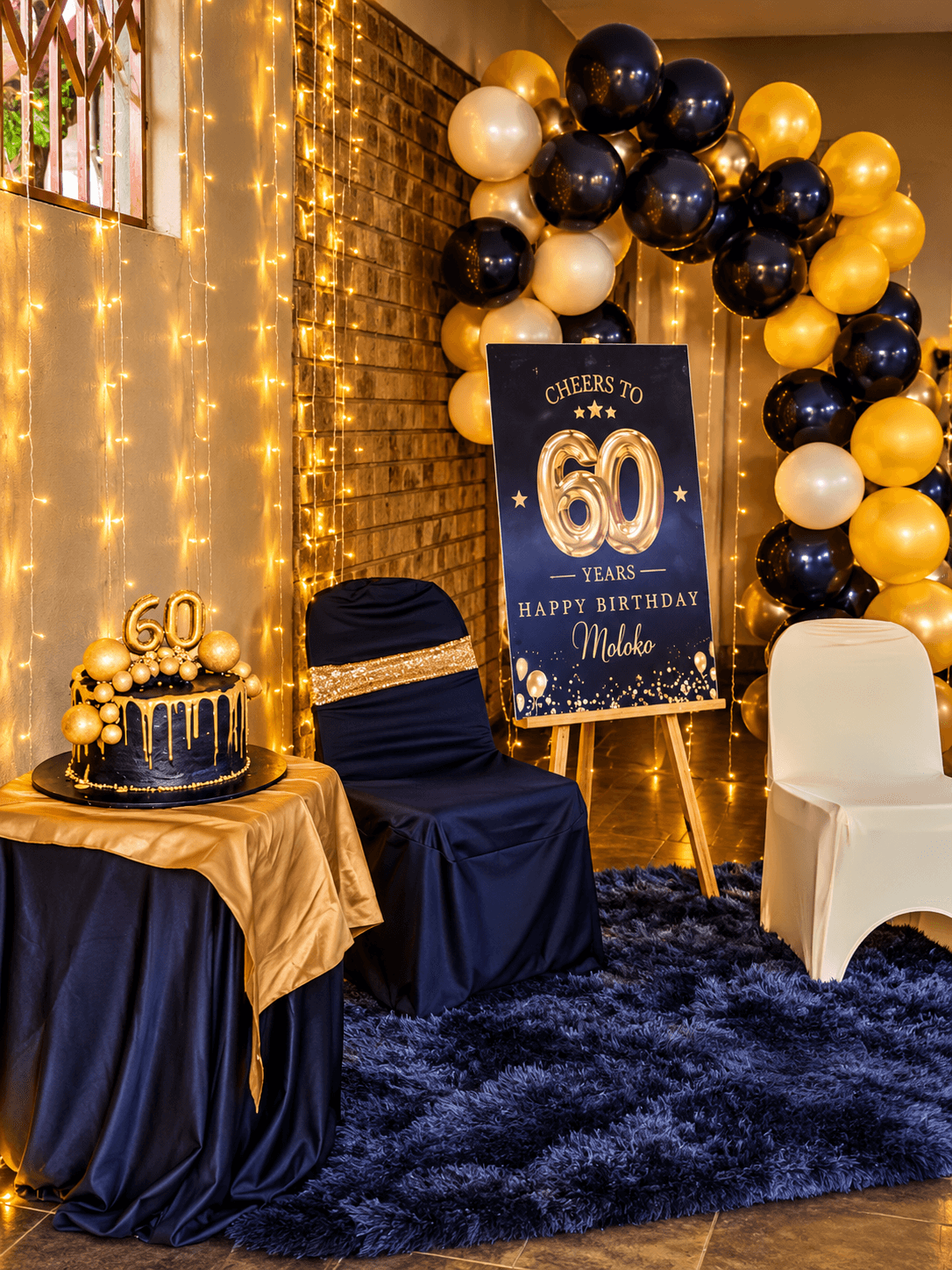 Navy and gold 60th birthday corner with a balloon arch, "Cheers to 60 Years" sign and a gold drip cake
