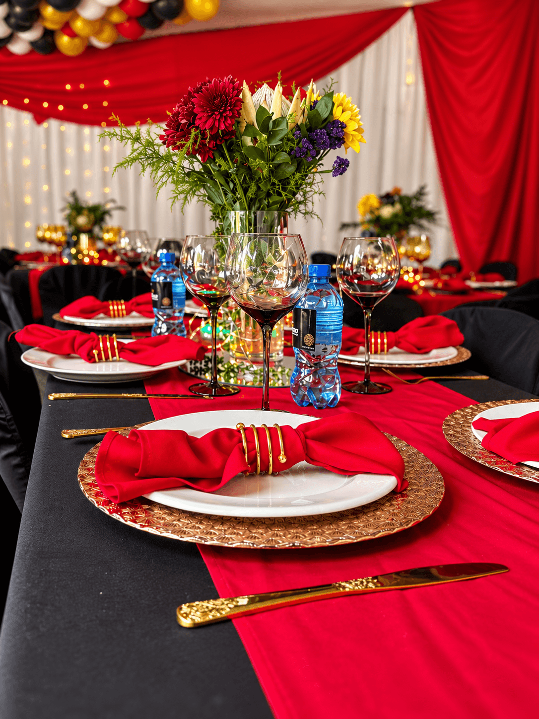 Red and gold banquet table set with gold chargers, gold cutlery, red napkins and a vibrant floral centrepiece